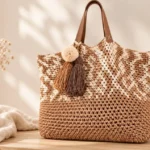 Gehäkelte Strandtasche mit Quasten in Hellbraun und Creme mit Lederhenkeln und Bommel, hängend an einem Haken